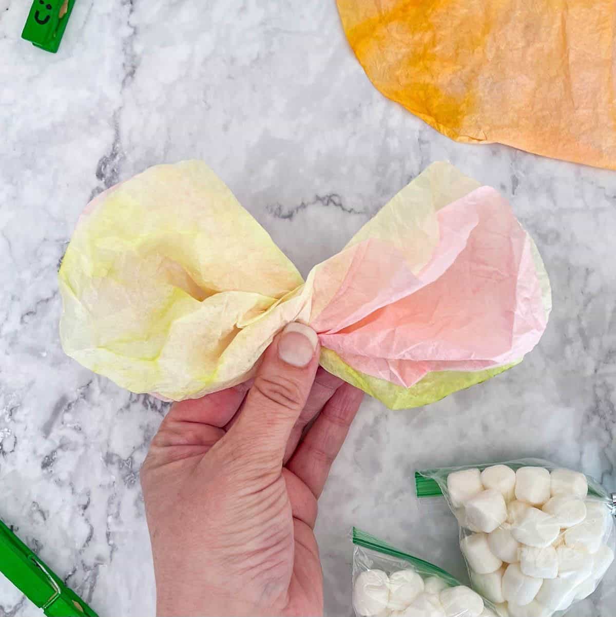 A woman's hand shows colored coffee filters twisted in half to create a two tone bow.